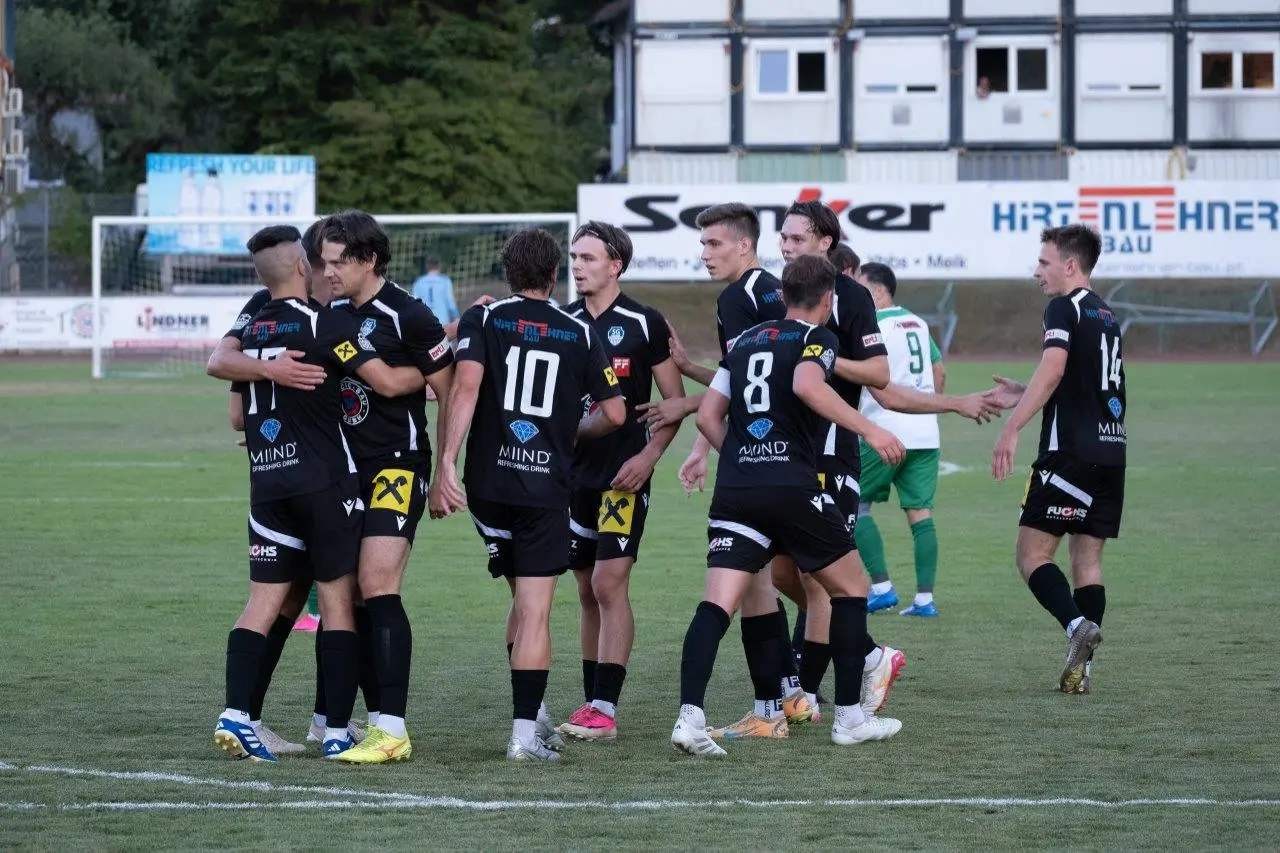 Fußballspieler in schwarzen Trikots umarmen sich auf einem Rasenplatz in Vorchdorf.